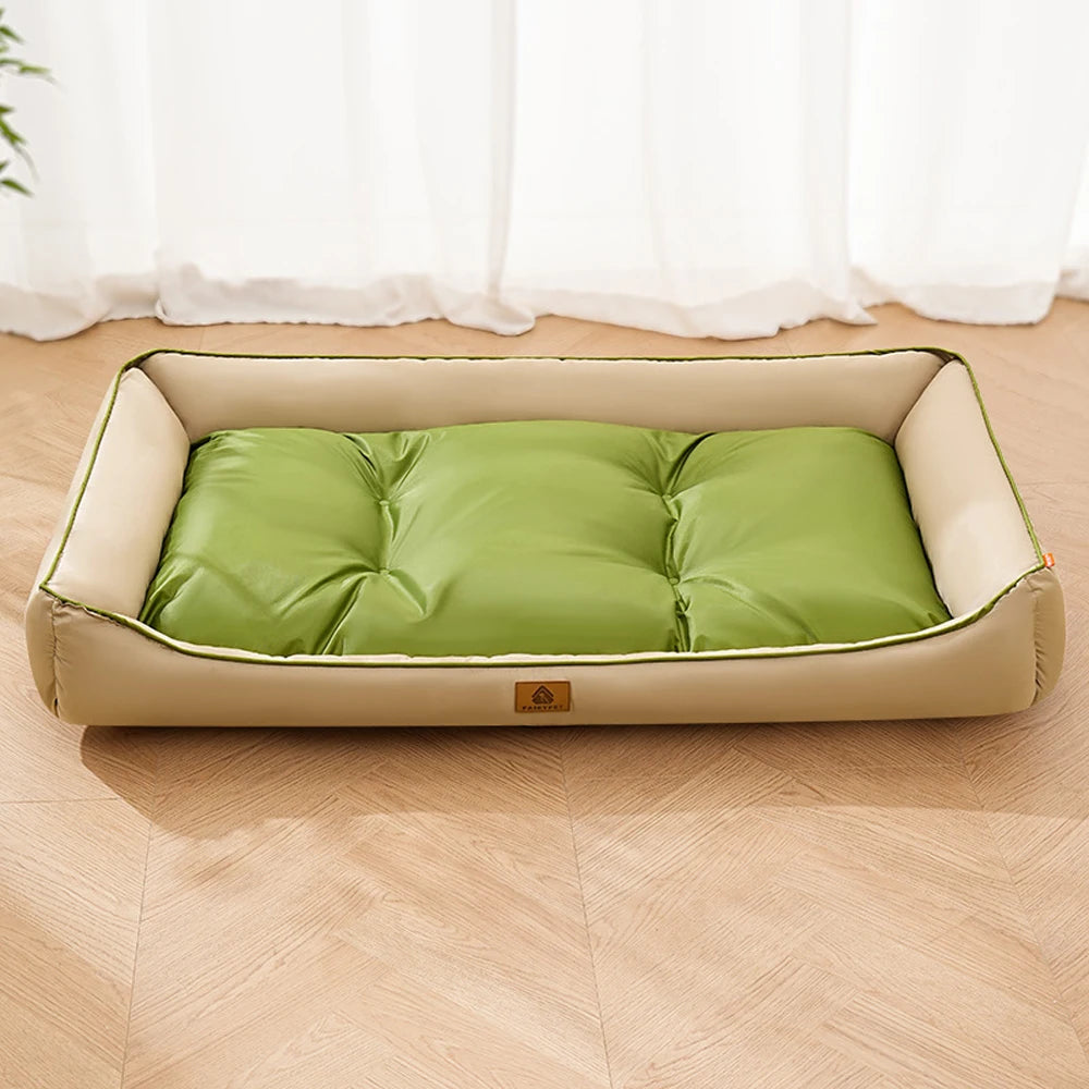 A light beige pet sofa bed with a green cushion is placed on a wooden floor in front of sheer white curtains.