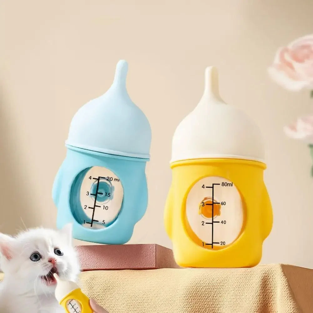A small white kitten is licking a yellow silicone pet nursing bottle with an anti-choking valve.