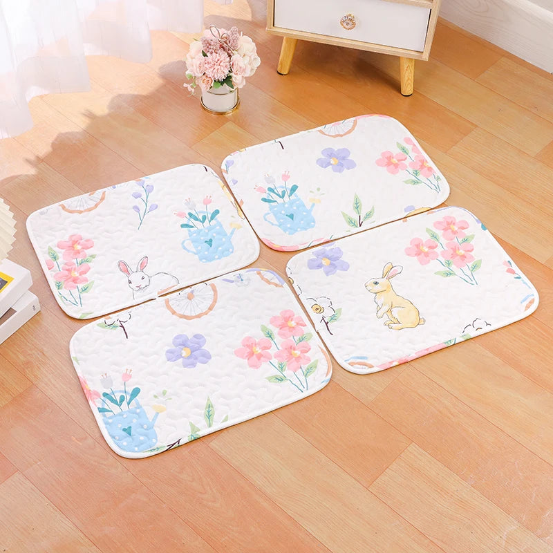 Four pink and purple floral patterned soft cotton pet cage mats with non-slip bases on a wooden floor.