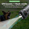 A hand holds a dog repellent device emitting a bright ultrasonic beam toward a dog in a grassy outdoor setting.