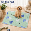 A golden retriever puppy is sitting on a green pet pee pad with blue and white heart shapes.