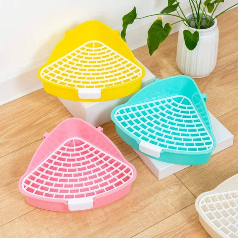 Three plastic litter boxes in yellow, teal, and pink are displayed on a wooden surface.