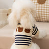 A fluffy white dog wearing a striped bear cardigan sweater with brown bear ears.