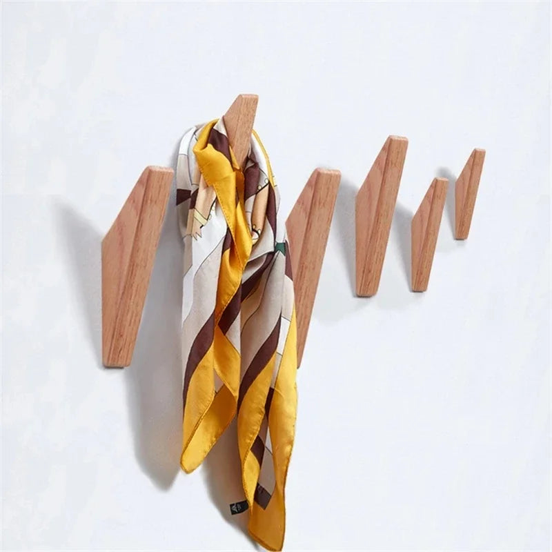 A yellow and brown striped scarf is displayed on a wooden wall mounted coat rack with three hooks.