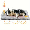 A fluffy black and white dog is lying on a gray pet bed mat with heat elements visible below.