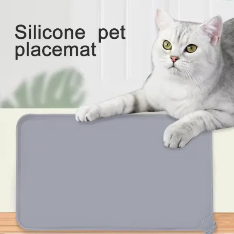 A gray cat is sitting on a smooth, rectangular silicone pet placemat.