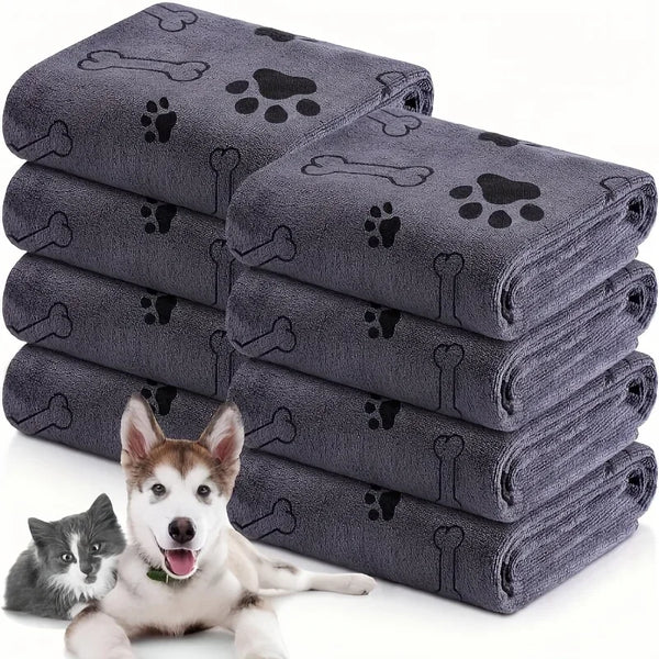 Stapel dunkelgrauer, ultraabsorbierender Mikrofaser-Haustierhandtücher mit Pfotenabdruck-Motiven neben einem Hund.