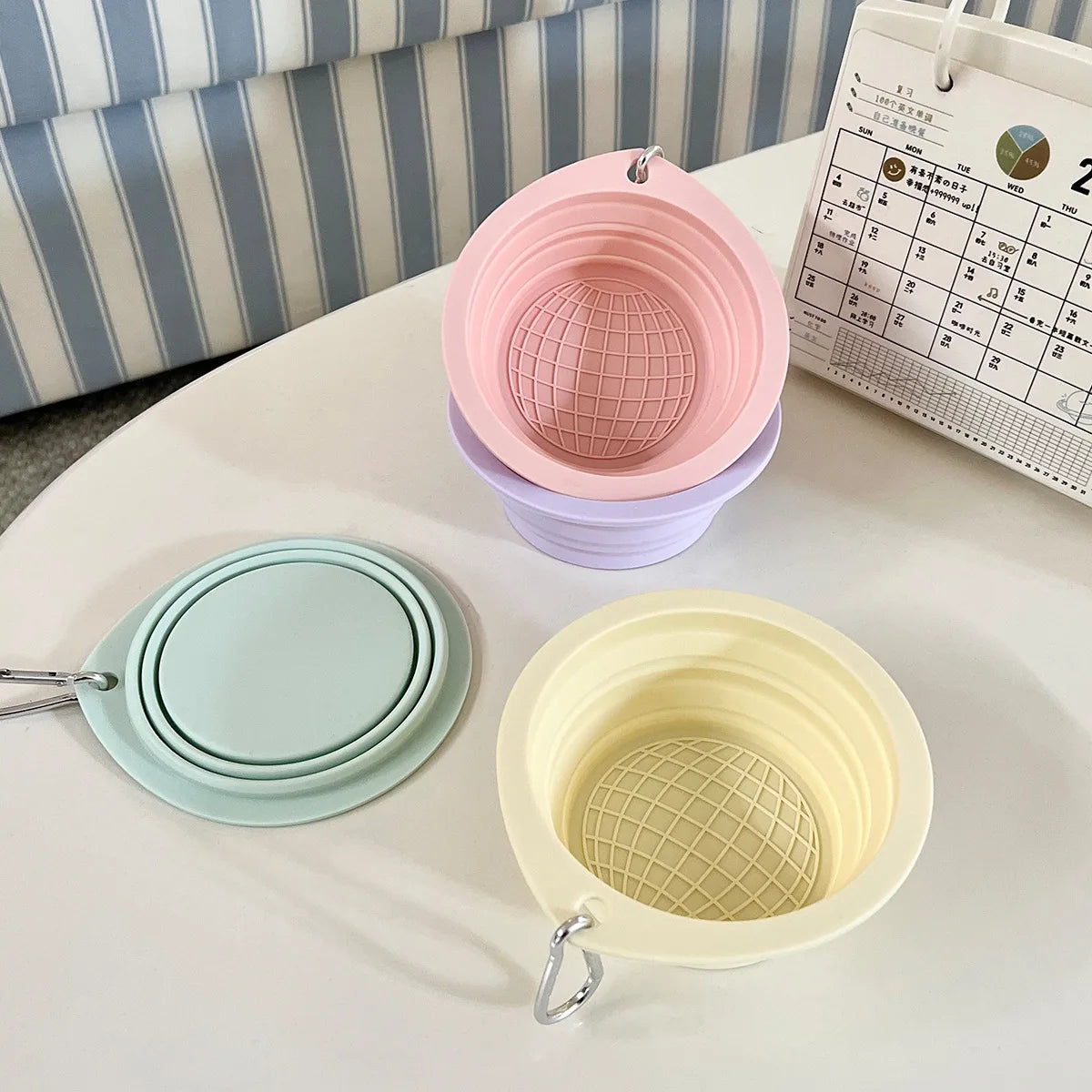 Two collapsible silicone pet travel bowls in pink and yellow are displayed on a white table.