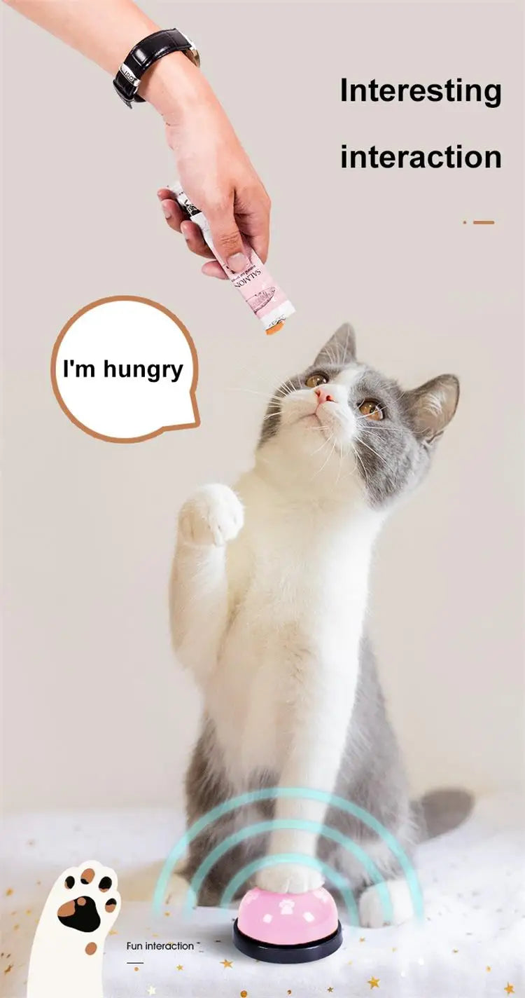 A fluffy gray and white cat looks up at a hand holding a small pink device, with a footprint training bell visible below.