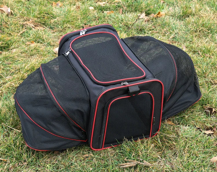 A black foldable soft-sided pet carrier lying on green grass.