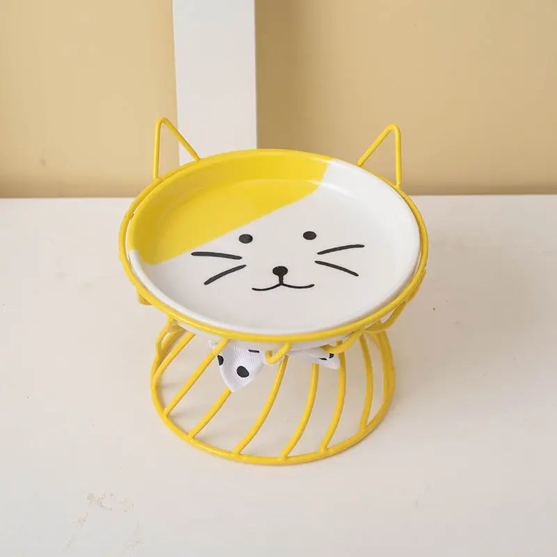 A yellow ceramic cat food dish with a white cat face design is shown on a white surface.