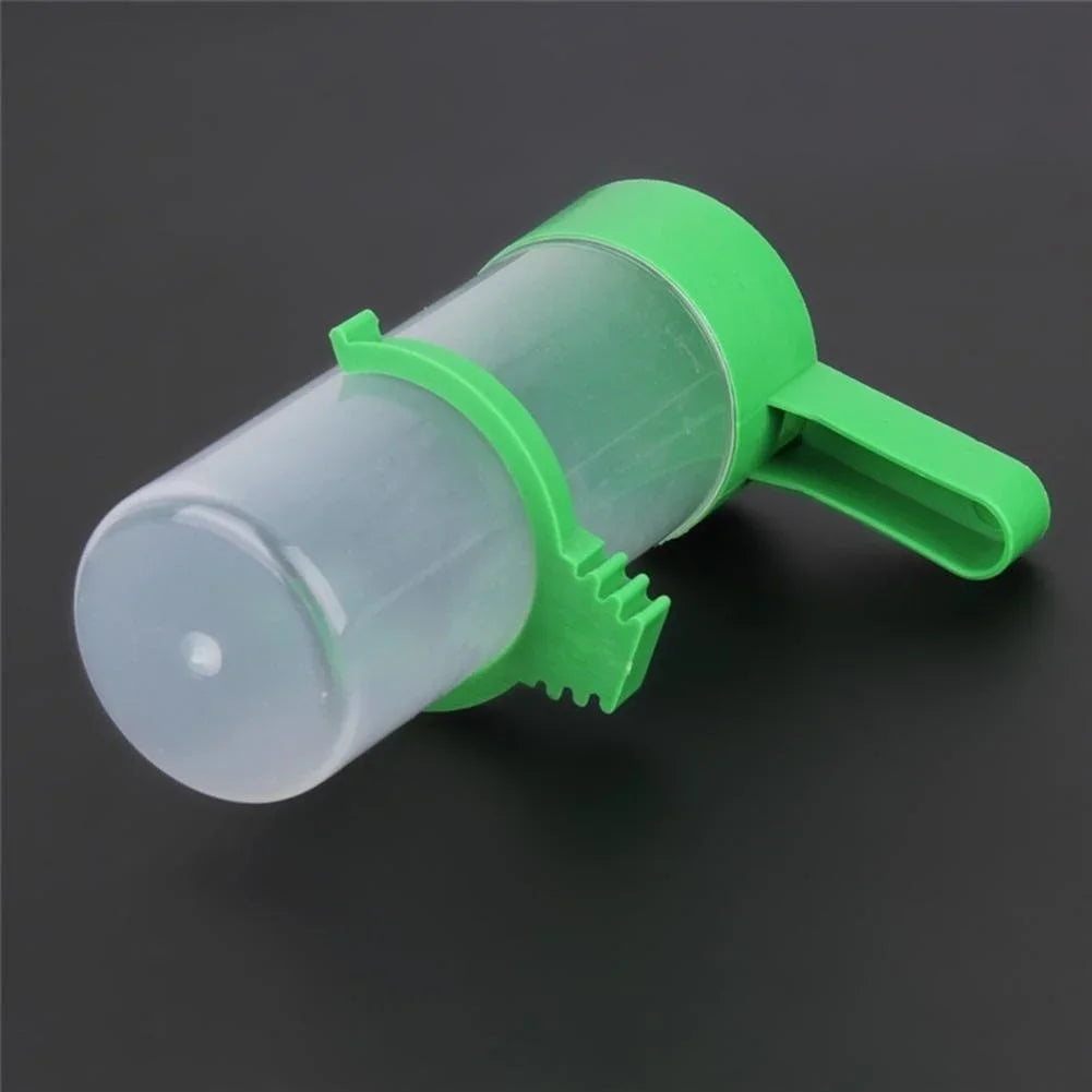 A green clip-on bird feeder and waterer set with a clear container, shown against a dark background.