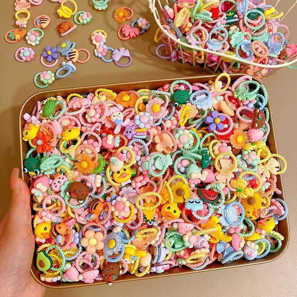 A tray filled with colorful cute cartoon elastic hair ties for kids in various shapes and colors.