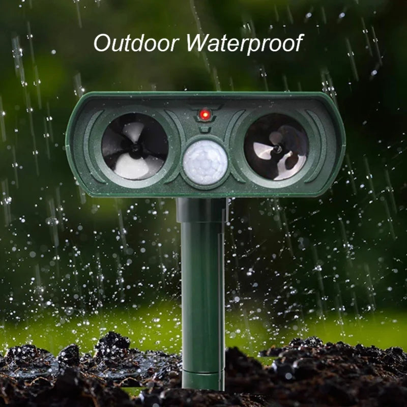 A green outdoor waterproof ultrasonic animal repeller device installed in dark soil under a rain shower.
