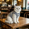 A fluffy gray cat wearing a navy blue and white striped knitted vest sitting on a wooden table.