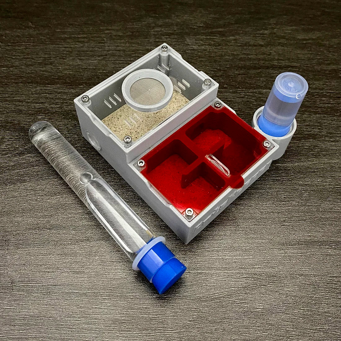 A clear plastic box containing a glass tube and a red compartment for observation, used as an ant observation farm.