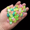 A hand holds a cluster of colorful glow-in-the-dark decorative stones in various shades of pink, green, and yellow.