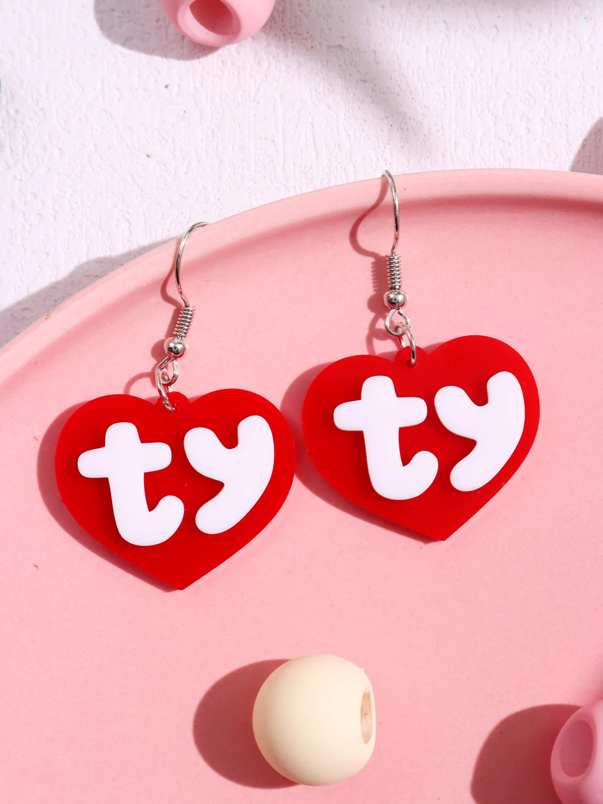 Pair of red acrylic heart stud earrings with white text TY