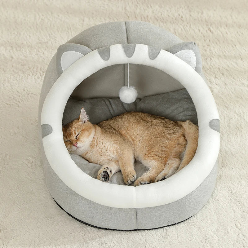 A fluffy orange tabby kitten is resting inside a gray and white cat cave bed with ear shapes.