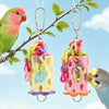 Two colorful plastic hanging toys shaped like blocks are suspended from a branch next to a parrot.