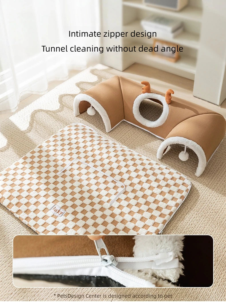 A tan plush cat bed featuring a reindeer tunnel design on a light rug.