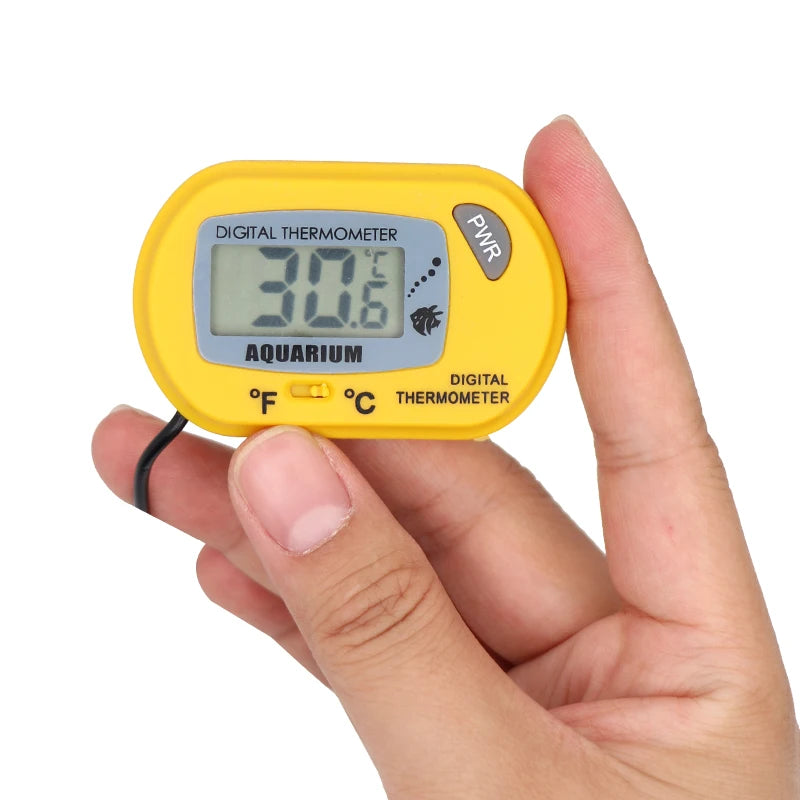 Eine Hand hält ein gelbes digitales Thermometer für ein Aquarium, das eine Temperatur von 30,6 Grad anzeigt.
