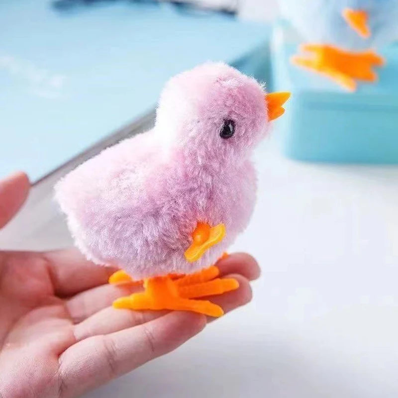 A small pink fluffy plush chick toy with orange feet is held in a person's hand.