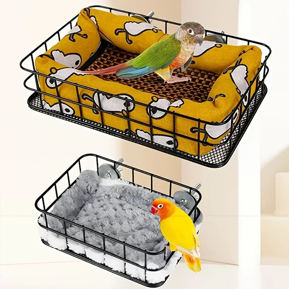 A black mesh parrot nest bed filled with yellow fabric and a green parrot, alongside a silver bird toy.