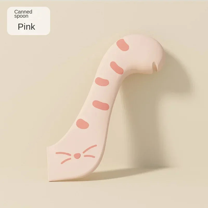 A pink canned spoon with a textured handle and a small cat-like shape is shown against a light background.