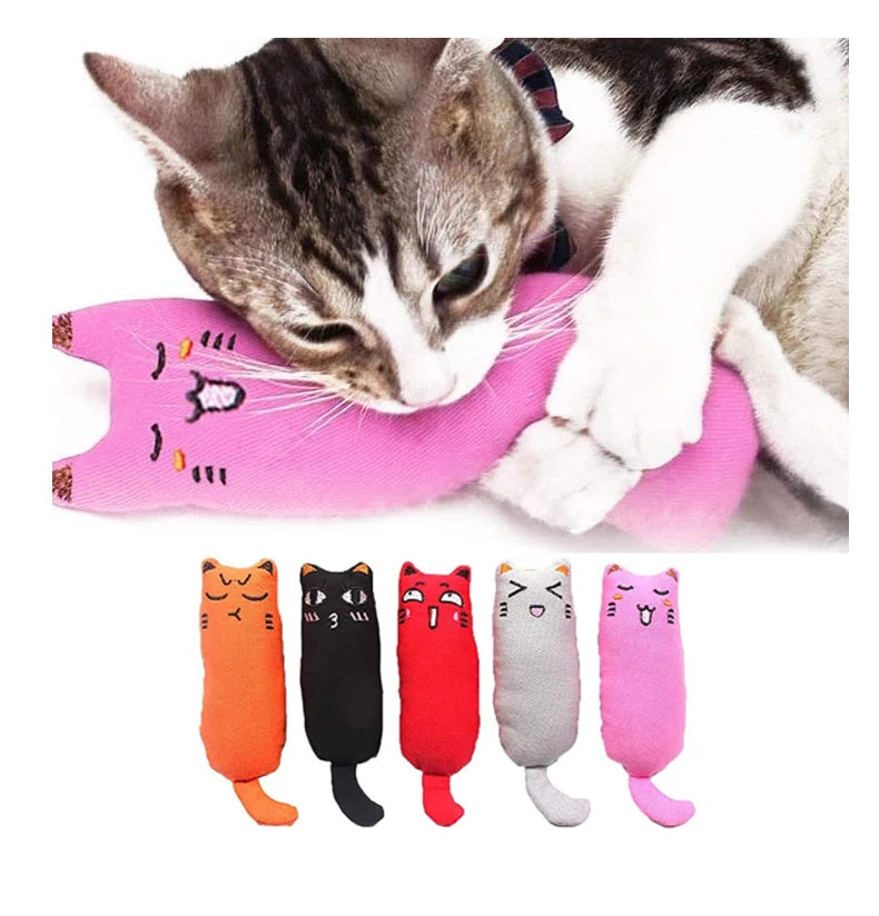 A fluffy gray and white cat is resting on a pink crinkle toy shaped like a cat's face, with several plush cat toys displayed 