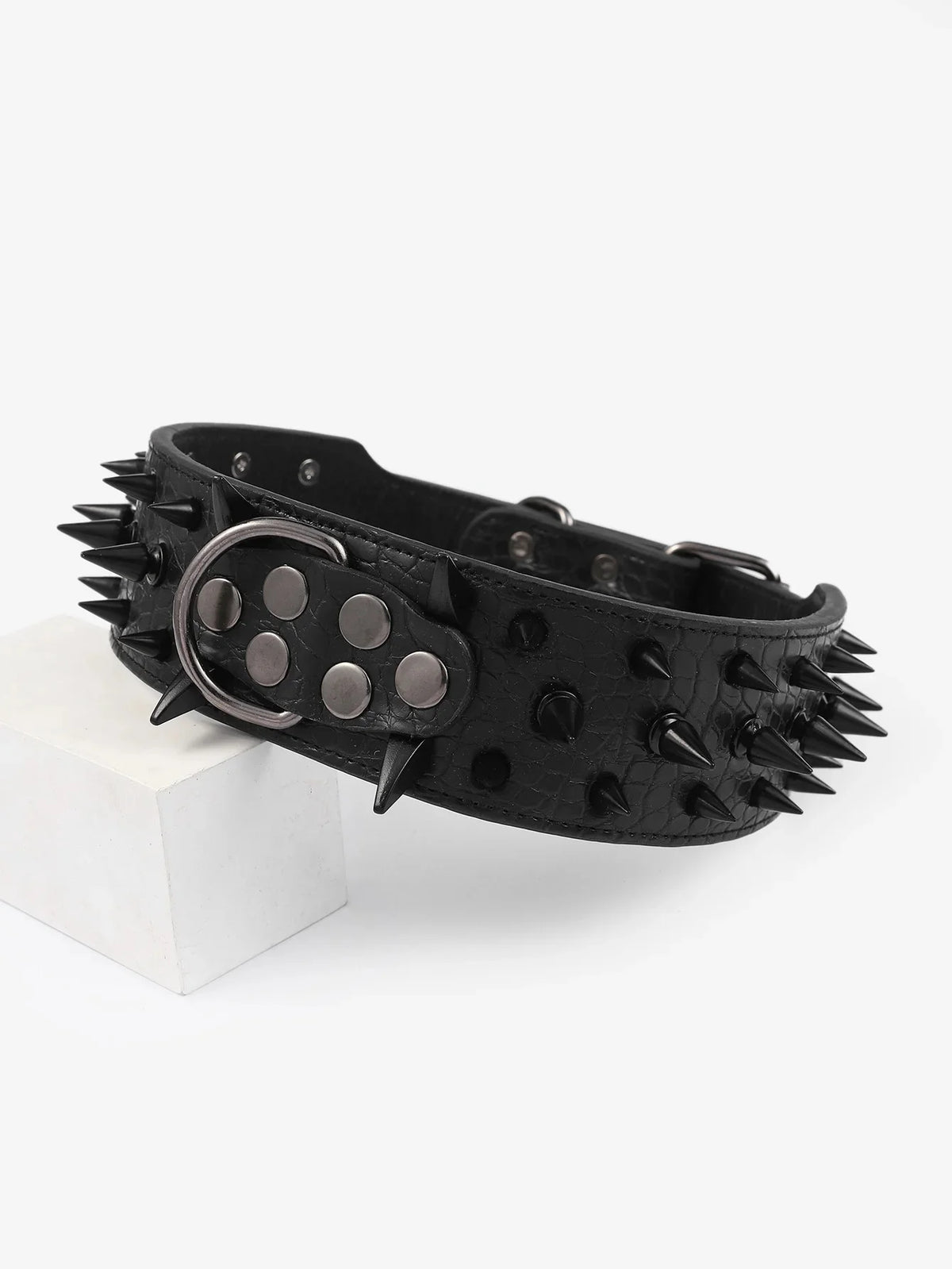 Black spiked leather dog collar with a silver buckle resting on a white block.