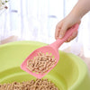 A hand is holding a pink plastic cat litter scoop filled with cat litter over a green bowl.