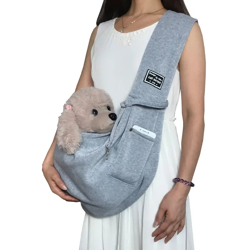 Eine Frau trägt einen grauen, leichten Pet-Crossbody-Sling-Träger mit einem schwarzen Etikett auf ihrem Oberkörper.