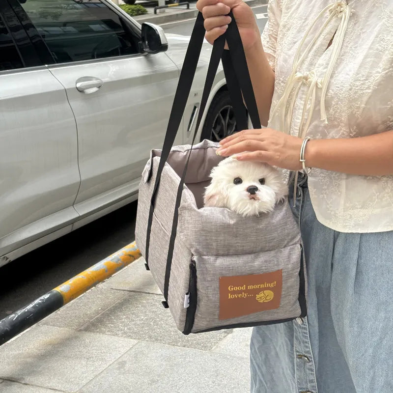 Eine Person hält ein graues, tragbares Hundesitzbett mit einem weißen, flauschigen Hund, neben einem silbernen Auto.
