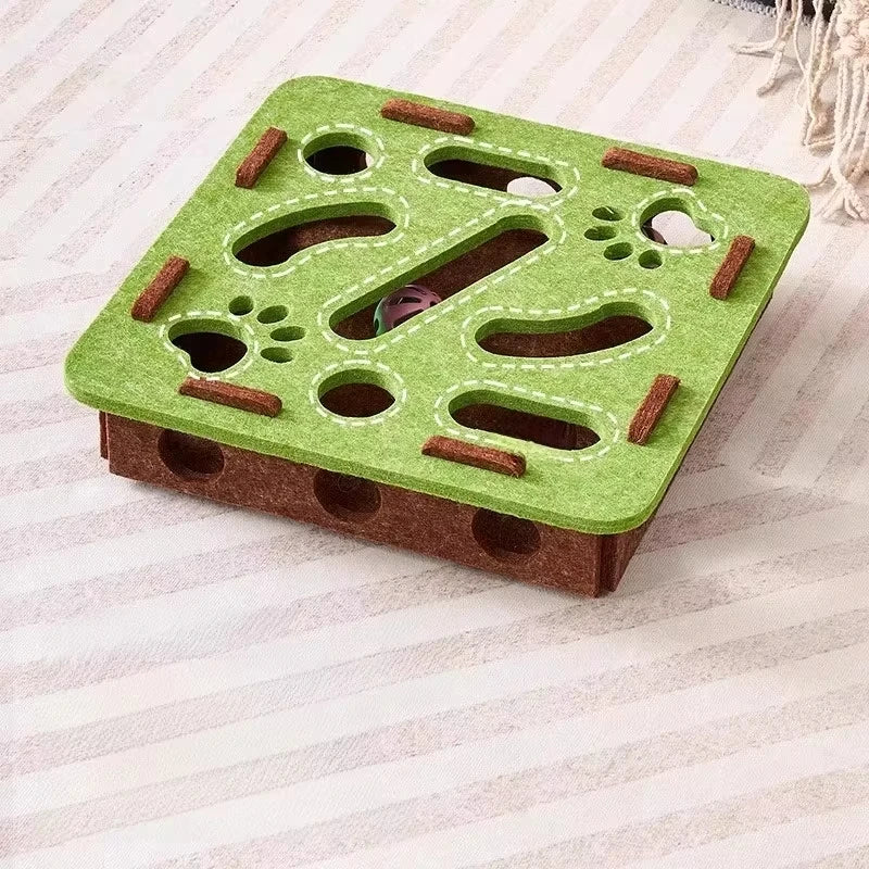 A green felt puzzle toy for cats with various holes and textured surfaces resting on a light fabric.