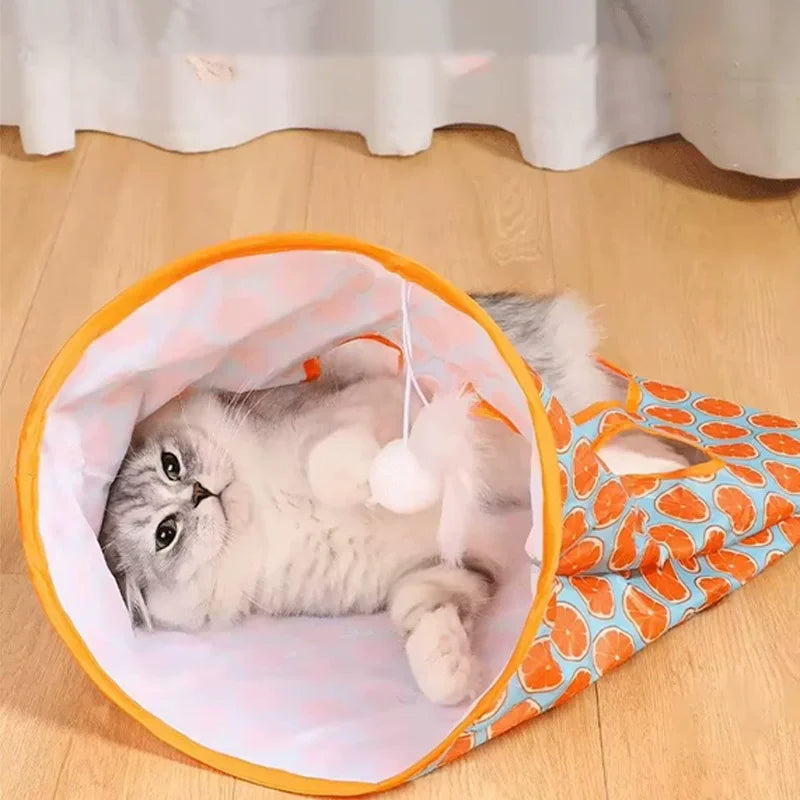 A fluffy white kitten is inside an orange and white crinkle fabric tunnel for play.