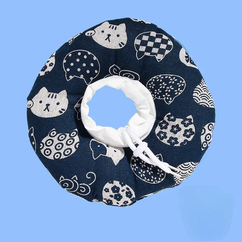 A dark blue fabric collar with a repeating pattern of white cat faces and paw prints, featuring a white adjustable loop.