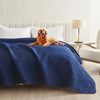 A golden retriever lies on a dark blue waterproof pet bed cover on a white sofa or mattress.