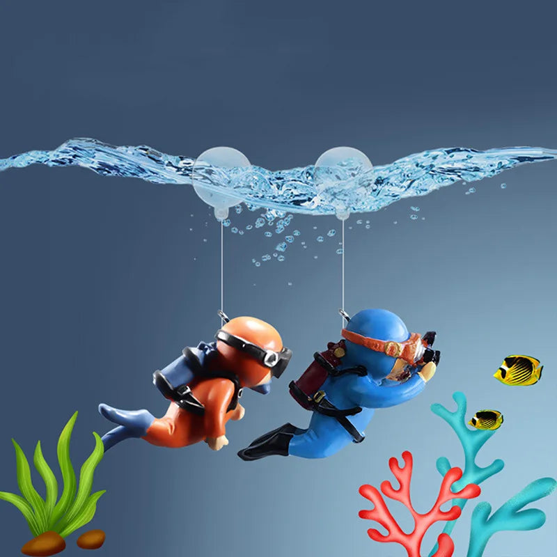 Two miniature diver figures are suspended by strings, with small floating balls and colorful coral decorations below.