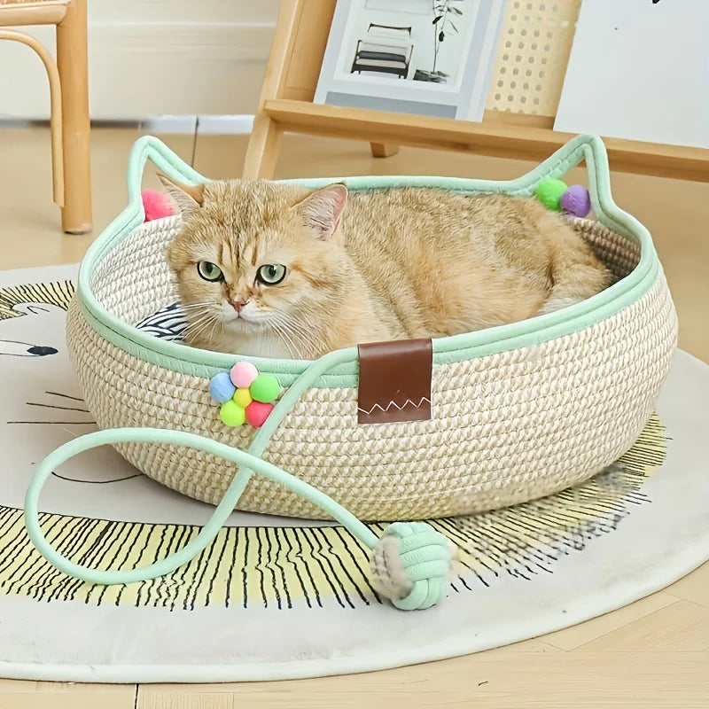 A light beige hand woven rattan cat bed with a green trim and a small orange tabby kitten resting inside.