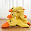 A yellow knitted plush duck toy with orange beak and feet sitting on a wooden surface.