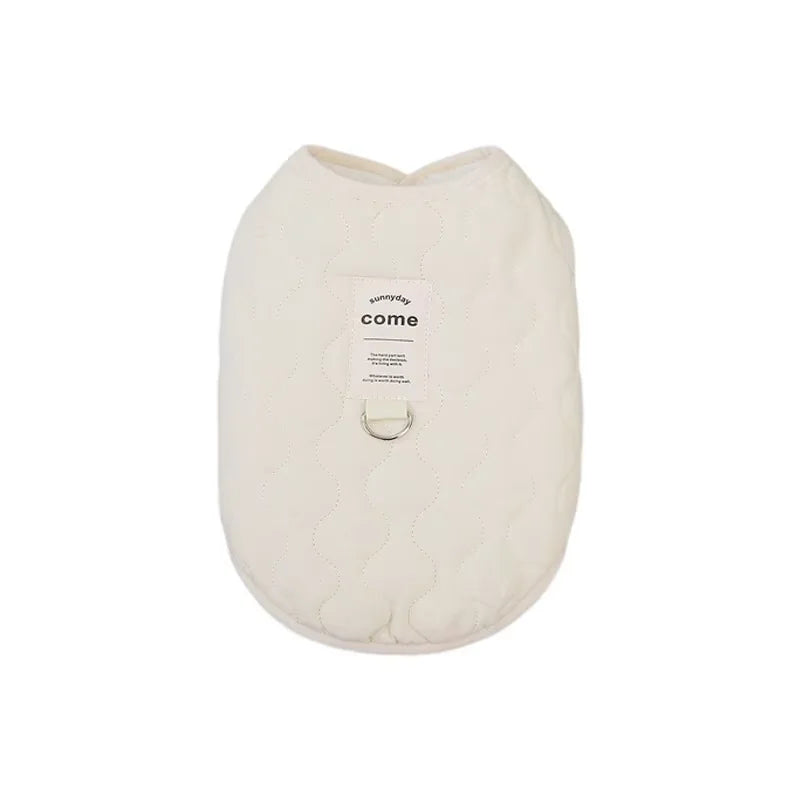 A cream-colored quilted pet vest with a small tag labeled come.