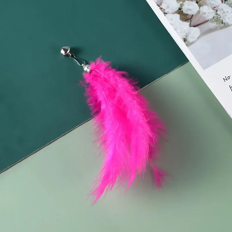 Leuchtend rosa Federspielzeug mit silberner Glocke und Clip, auf grüner Oberfläche.