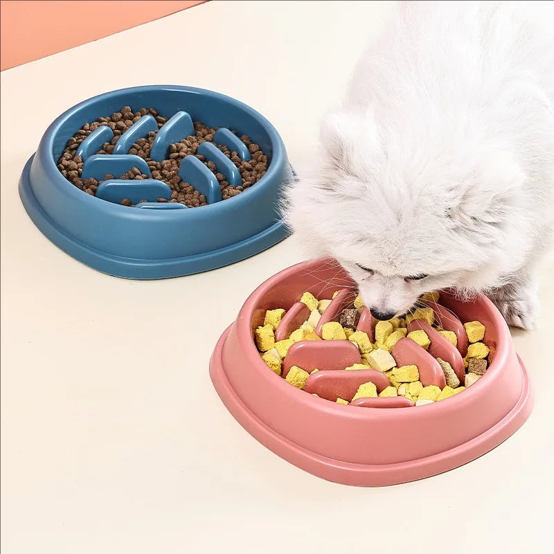 A white dog is eating food from a pink slow feeder bowl filled with kibble and meat pieces.