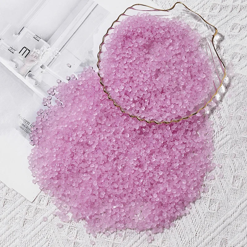 A pile of pink glow-in-the-dark decorative pebbles in a glass bowl on a white textured surface.