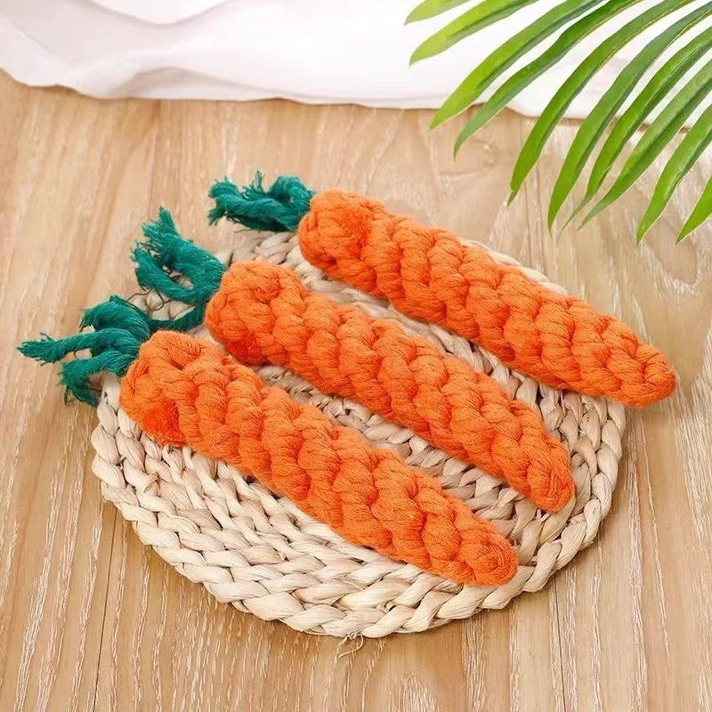 Orange plush carrot teething toy with green leaves resting on a woven mat