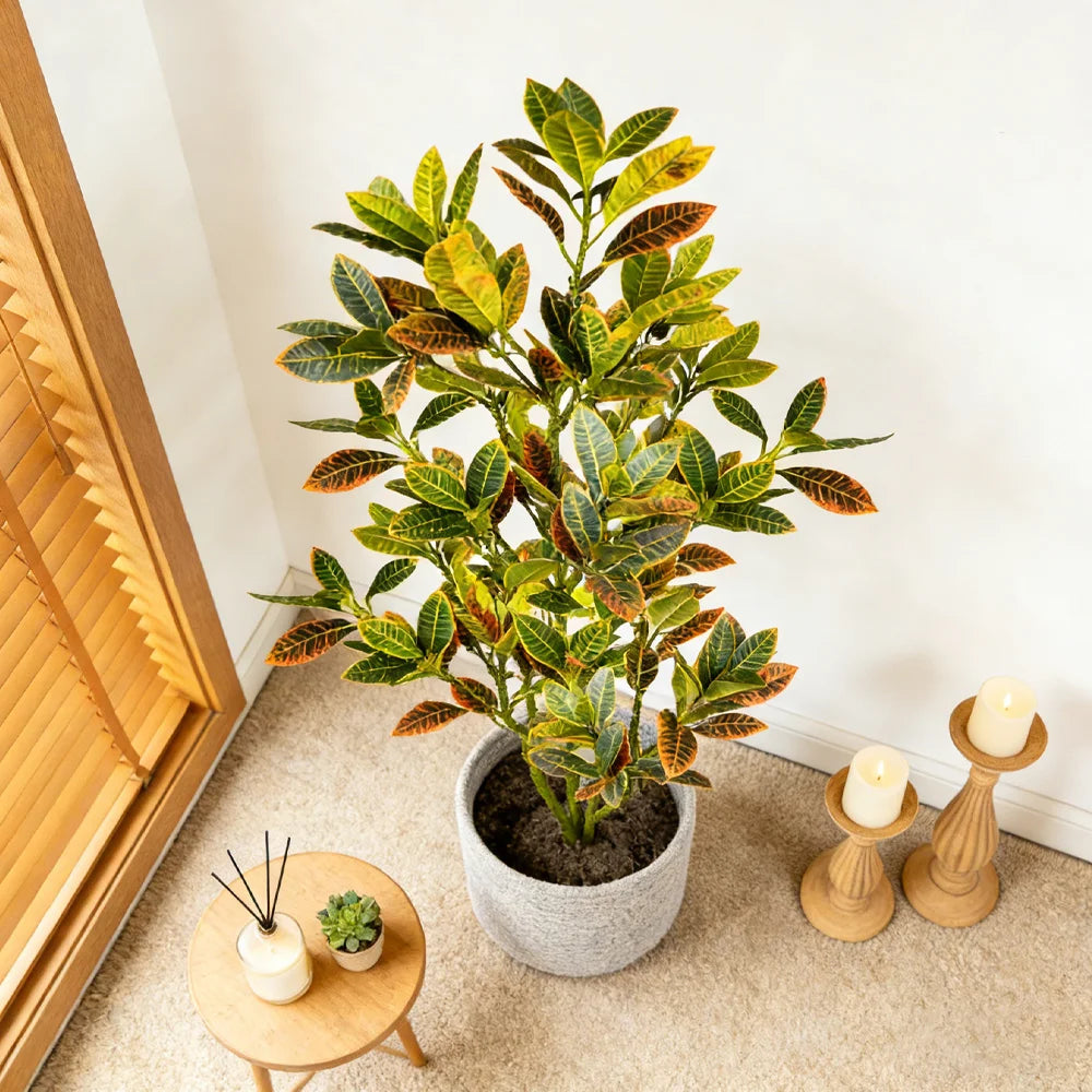 An artificial croton tree with vibrant green and yellow tropical leaves potted in a gray ceramic pot.