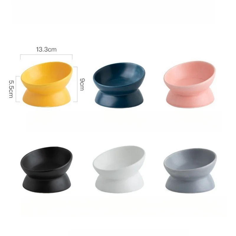 A set of four tilted ceramic cat bowls in yellow, dark blue, pink, and gray with raised stands.