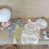 A collection of light-colored knitted mini vests and a white balloon on a wooden surface.