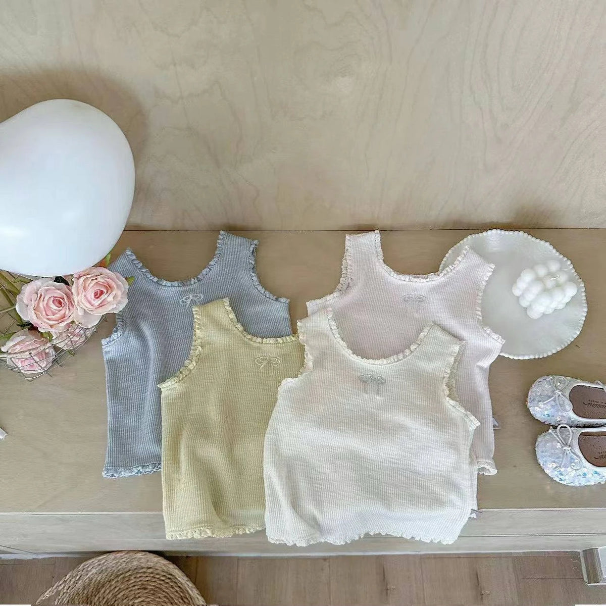A collection of light-colored knitted mini vests and a white balloon on a wooden surface.
